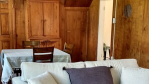 A room with a sofa, a dining table, and wooden walls.