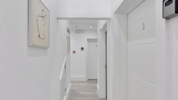 A hallway with a wooden floor, white walls, and a framed artwork on the left. - Harlesden Comfort Studio (London)