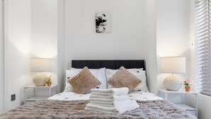 A neatly made bed with a fluffy blanket, two bedside tables with lamps, and a wall-mounted artwork. - Harlesden Comfort Studio (London)