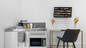 A modern kitchen with a built-in oven, a coffee maker, and a sink. There is a dining table with a chair and a vase with dried plants. - Harlesden Comfort Studio (London)