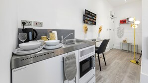 A modern kitchen with a built-in oven, a sink, and a dining area with a chair. - Harlesden Comfort Studio (London)