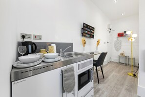 A modern kitchen with a built-in oven, a sink, and a dining area with a chair. - Harlesden Comfort Studio (London)