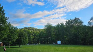 A grassy field with a white RV and a small building, surrounded by trees. - Secluded Vermont Escape – Mins to River, Trails, & Foliage (Sharon)