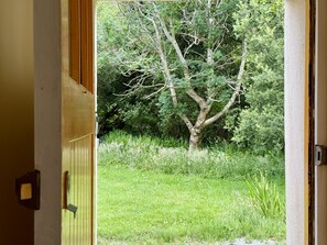 Une porte ouverte donnant sur un arbre et de l’herbe.