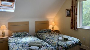 Ein Schlafzimmer mit zwei Betten, einem Fenster mit Vorhängen, einer Deckenleuchte und einem Nachttisch mit Lampe.
