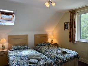 Ein Schlafzimmer mit zwei Betten, einem Fenster mit Vorhängen, einer Deckenleuchte und einem Nachttisch mit Lampe.