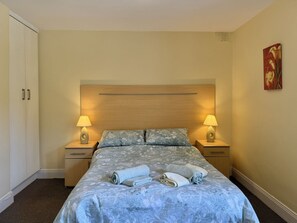 Une chambre d’hôtel avec un lit, deux tables de chevet, une tête de lit et un tableau au mur.