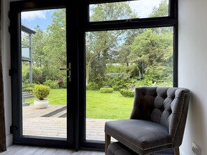 Een kamer met een grote schuifglazen deur die uitkomt op een tuin met gazon, potplanten en een houten terras.
