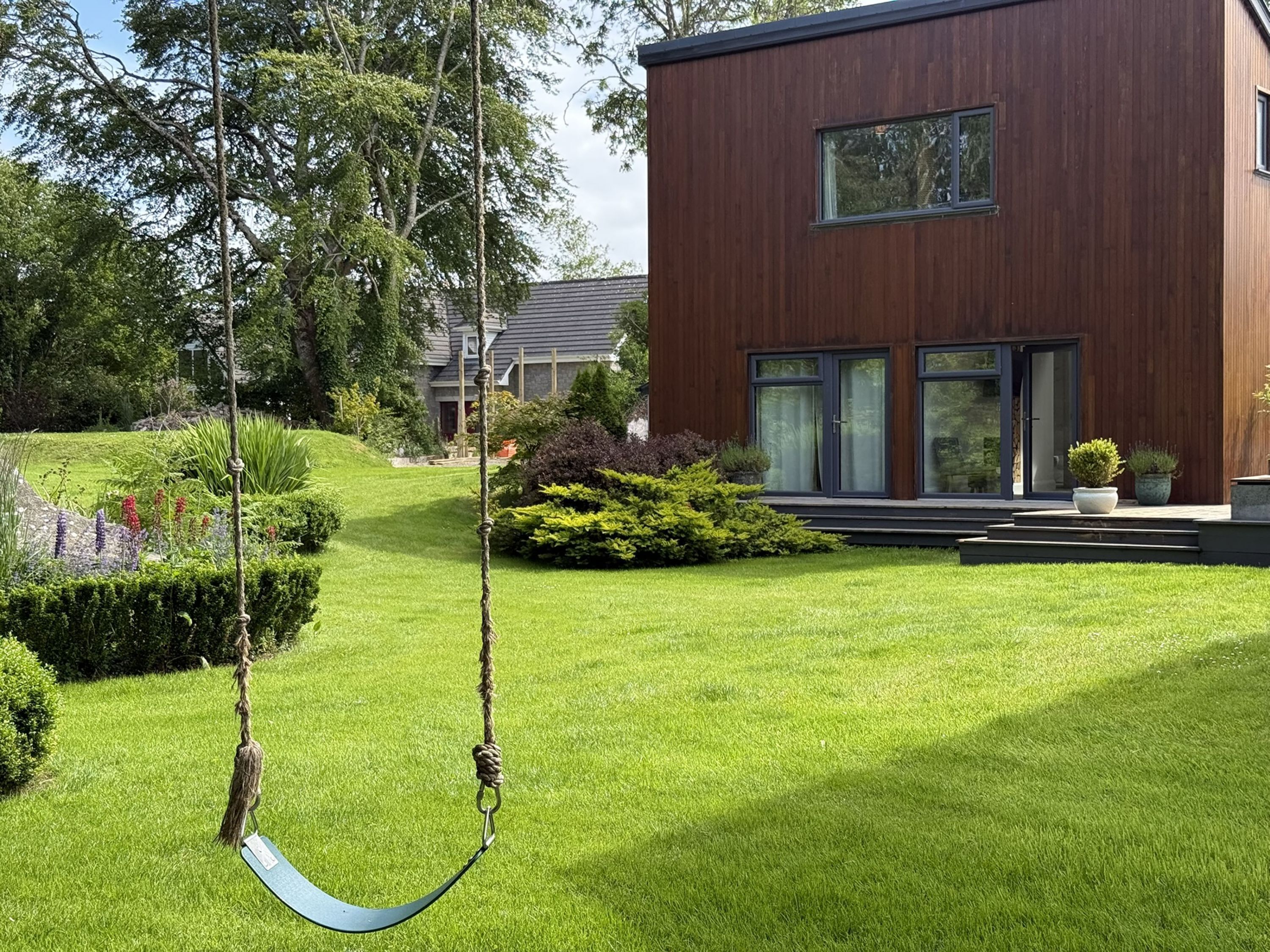 Une maison moderne avec une pelouse bien entretenue, une balançoire et un jardin où poussent différentes espèces de plantes.