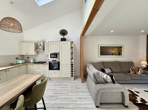 A modern kitchen with white cabinets, a dining table, and a gray sofa in the living area.