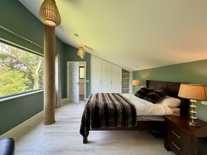 Een slaapkamer met een bed, nachtkastje, lamp en een groot raam.