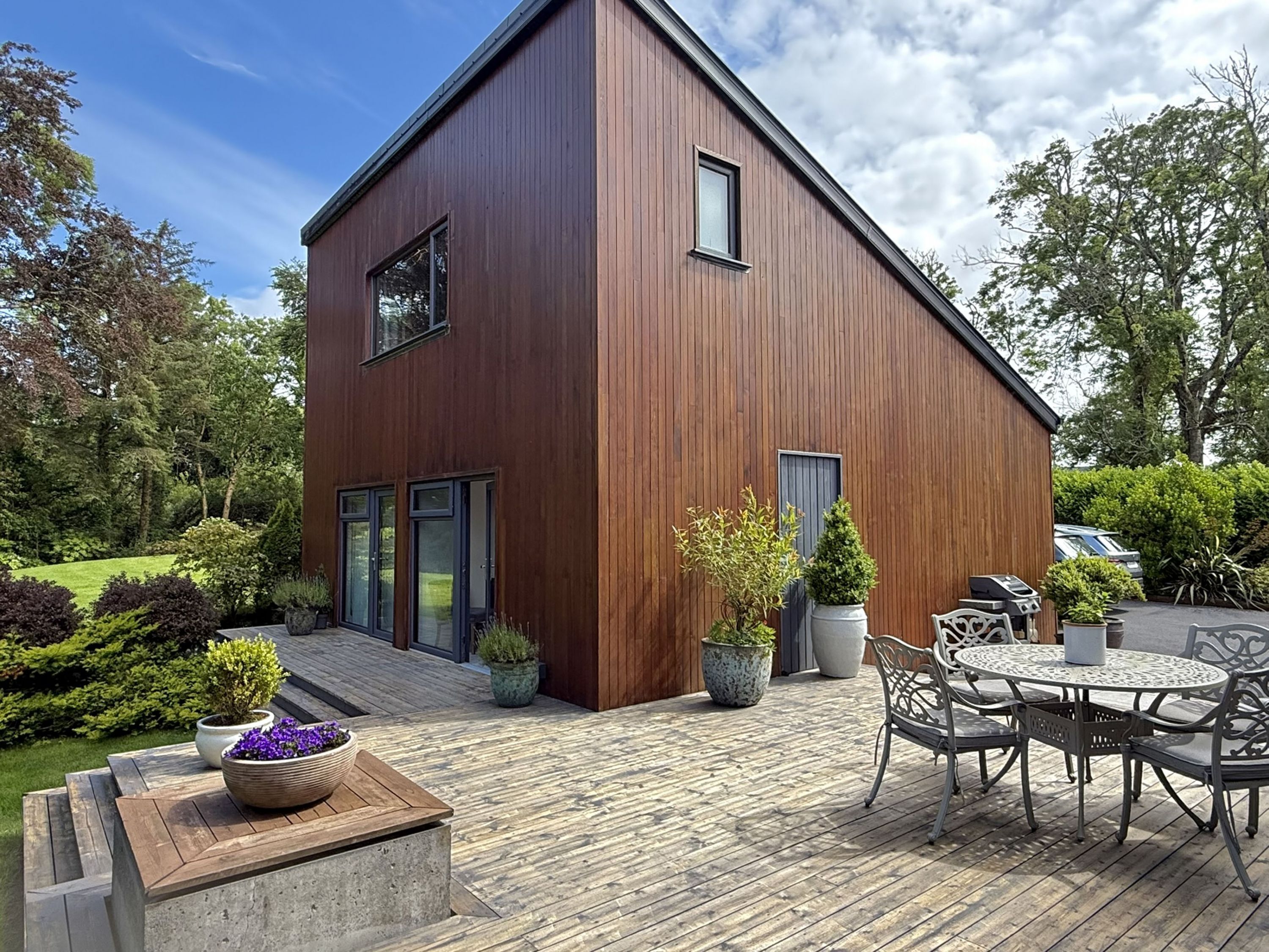 A modern wooden building with a deck, outdoor seating, and potted plants.