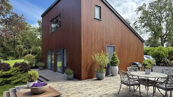 A modern wooden building with a deck, outdoor seating, and potted plants.