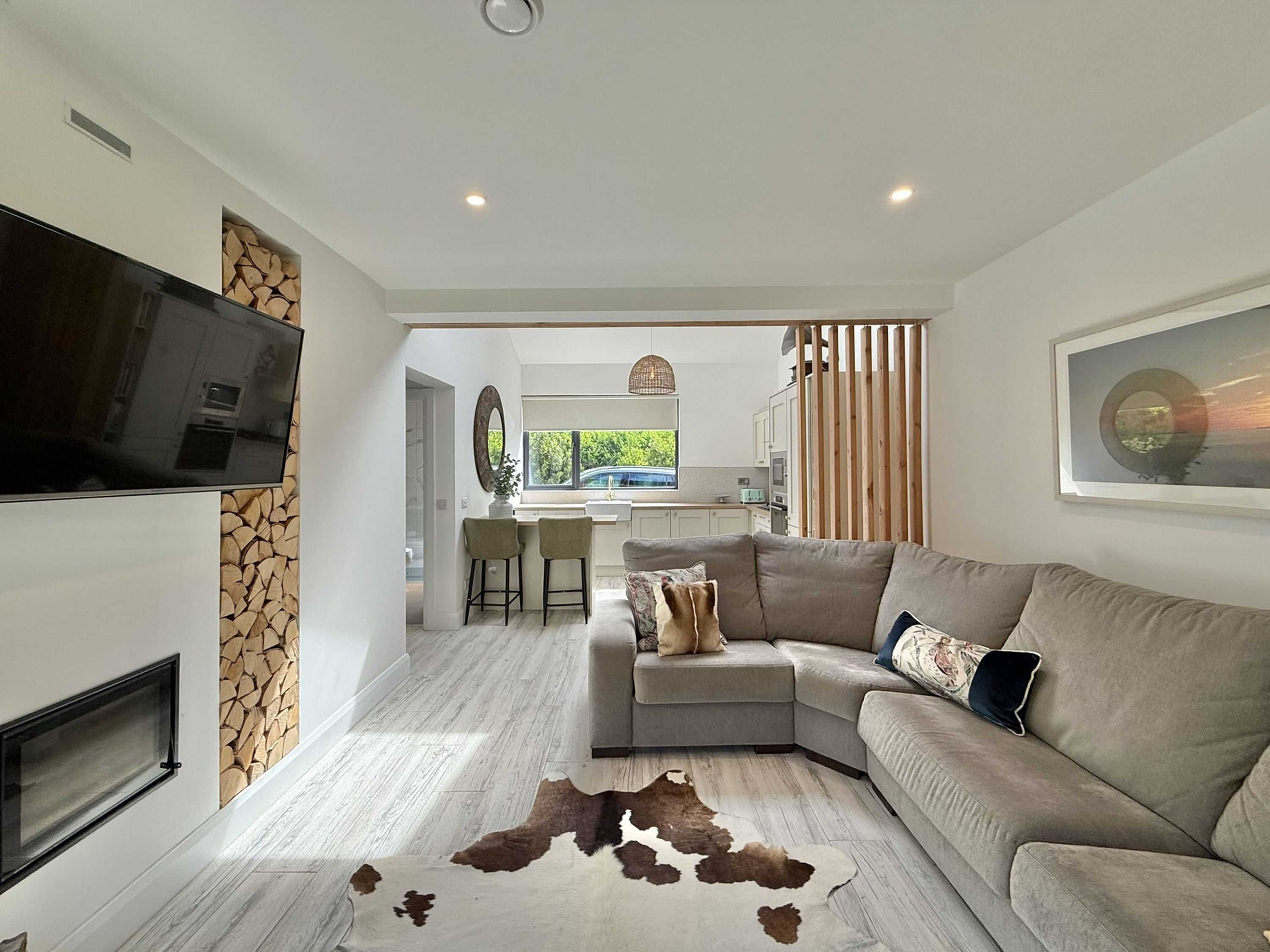 Un salon moderne avec un canapé d’angle, un téléviseur à écran plat fixé au mur, une cheminée et un tapis en peau de vache.