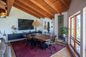 Un coin repas avec une table en bois, des chaises noires, un tapis rouge et une grande fenêtre donnant sur un beau paysage.