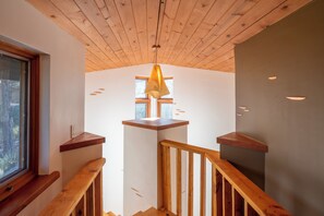 Eine Holztreppe mit Holzgeländer, einer hängenden Leuchte und einem Fenster mit Blick auf Bäume.