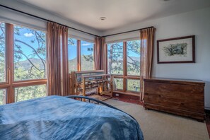 Une chambre avec un lit, une commode en bois et une fenêtre donnant sur des arbres et des collines.