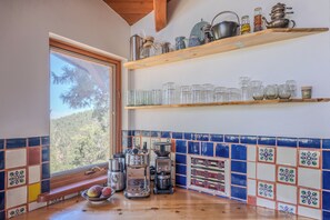Une cuisine avec une fenêtre, des étagères en bois, une machine à café et un grille-pain.