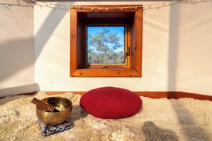 Ein kleiner Raum mit einem Holzfenster, einem roten Kissen und einer Messingschale auf einem flauschigen Teppich.