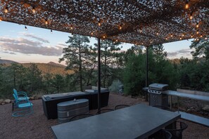 Een terras buiten met een pergola, zitplaatsen en een barbecue.