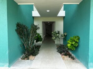 A corridor with a tiled floor, flanked by green plants and walls painted in a teal color. - Cozy 2BR Condo | Pool | FREE Electricity (Punta Cana)