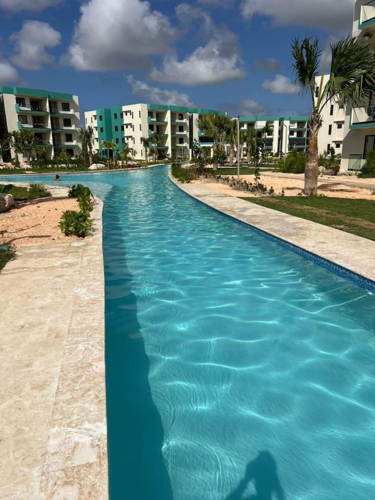 Une piscine à l’eau d’un bleu limpide, entourée d’une terrasse carrelée et bordée d’une rangée d’immeubles dotés de balcons.