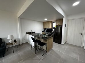 A modern kitchen with a central island, bar stools, and a dining area with a lamp. - Cozy 2BR Condo | Pool | FREE Electricity (Punta Cana)