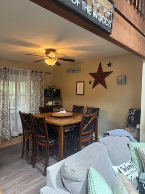 A dining area with a wooden table and chairs, a ceiling fan, and wall decorations including a star and a sign that says 'Lovin' Life by the Lake.'