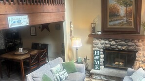 A cozy living room with a fireplace, a wooden staircase, and a dining area. - Shady Leaf Lodge - Family and pet-friendly! Arrowhead Lake getaway (Pocono Lake)