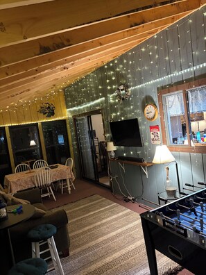 Ein gemütliches Zimmer mit Kicker, Fernseher und Essbereich mit Stühlen und Tisch.