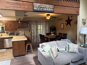 A cozy cabin interior with a kitchen, dining area, and a living room with a couch and decorative pillows.