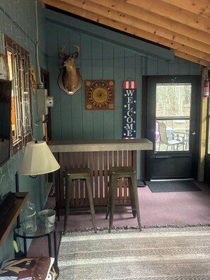 Un intérieur en bois, orné d’une tête de cerf accrochée au mur, d’une enseigne de bienvenue et d’un coin bar avec des tabourets.