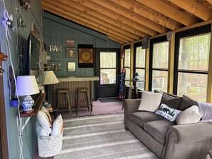 Ein gemütliches Blockhauss-Interieur mit Barbereich, einer Couch mit Zierkissen und großen Fenstern, die einen Blick ins Freie ermöglichen.