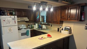 A kitchen with wooden cabinets, a white refrigerator, a stove, and a countertop with a bowl of tomatoes. - Shady Leaf Lodge - Family and pet-friendly! Arrowhead Lake getaway (Pocono Lake)