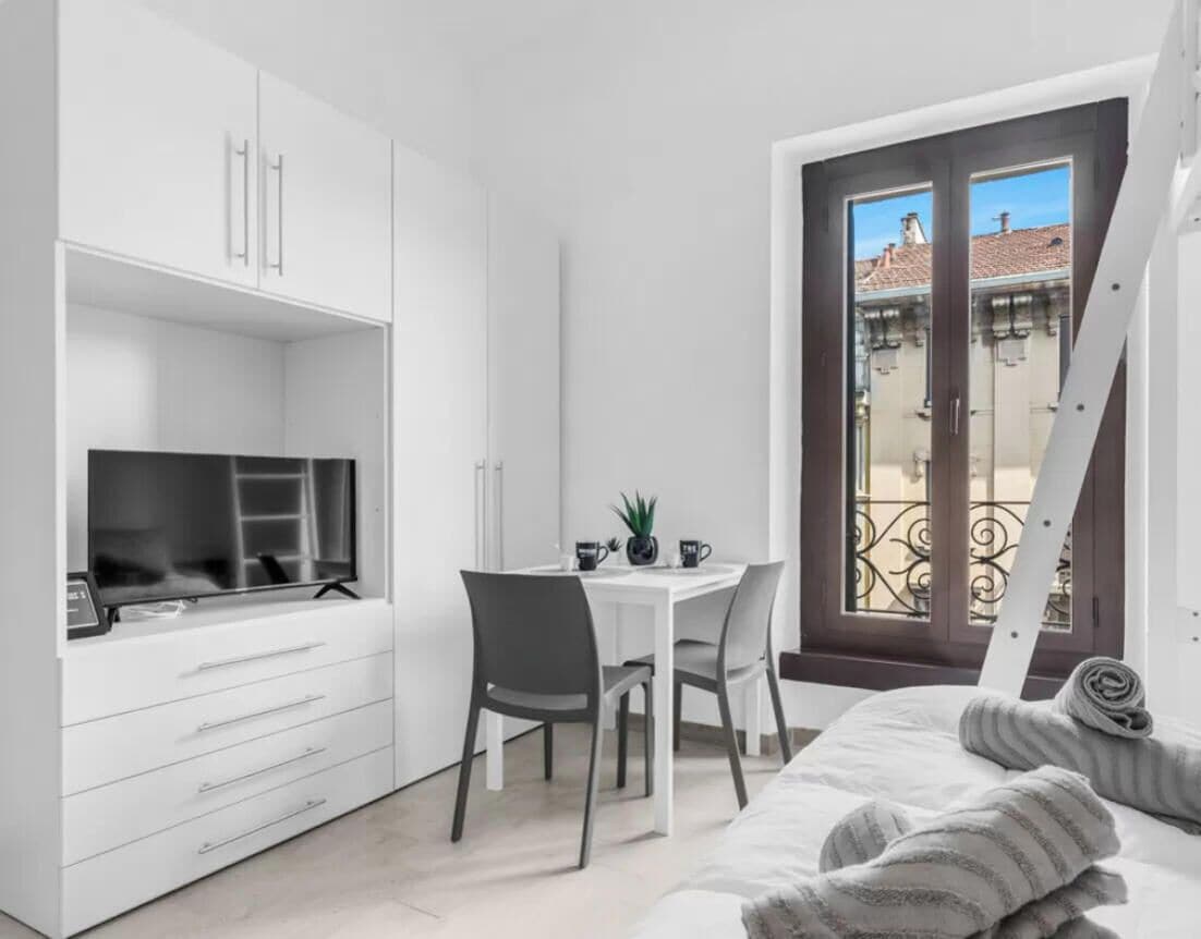 A compact room with a bed, a desk, and a window with a view of buildings.