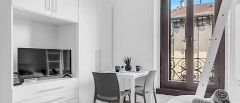 A compact room with a bed, a desk, and a window with a view of buildings.
