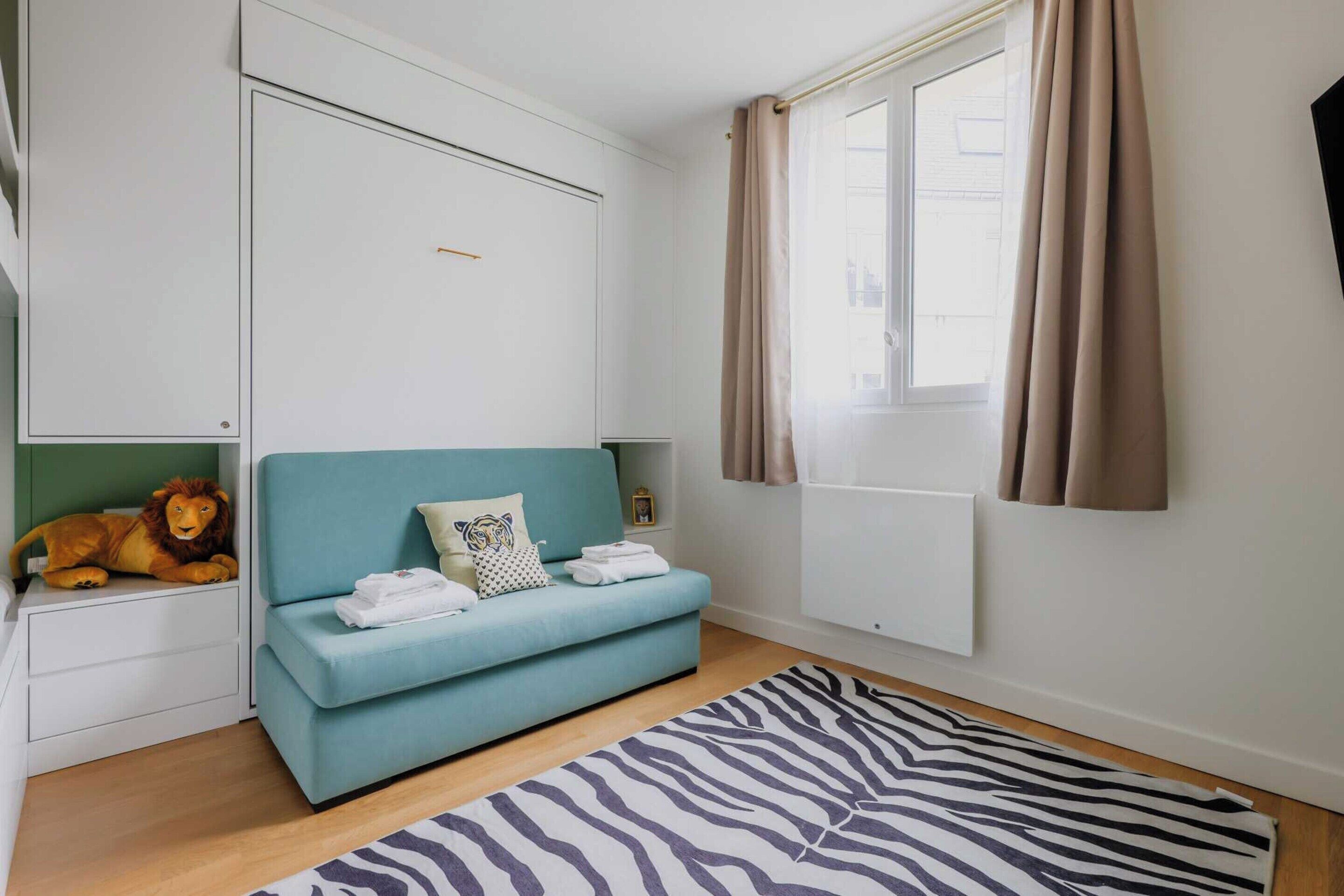A room with a teal sofa, a zebra-patterned rug, a lion decoration, a white cabinet, and a window with curtains.