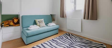 A room with a teal sofa, a zebra-patterned rug, a lion decoration, a white cabinet, and a window with curtains.