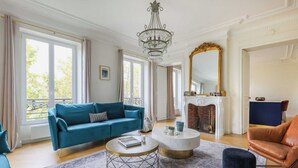 A spacious living room with a blue sofa, a round coffee table, and a fireplace. - Luxurious Apartment - 4br/10p- Ternes/pereire (Paris)