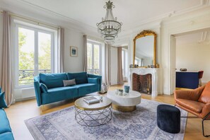 A spacious living room with a blue sofa, a round coffee table, and a fireplace. - Luxurious Apartment - 4br/10p- Ternes/pereire (Paris)