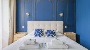 A bed with a tufted headboard, two bedside tables with lamps, and a blue wall with decorative paneling. - Luxurious Apartment - 4br/10p- Ternes/pereire (Paris)