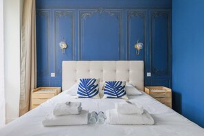 A bed with a tufted headboard, two bedside tables with lamps, and a blue wall with decorative paneling. - Luxurious Apartment - 4br/10p- Ternes/pereire (Paris)