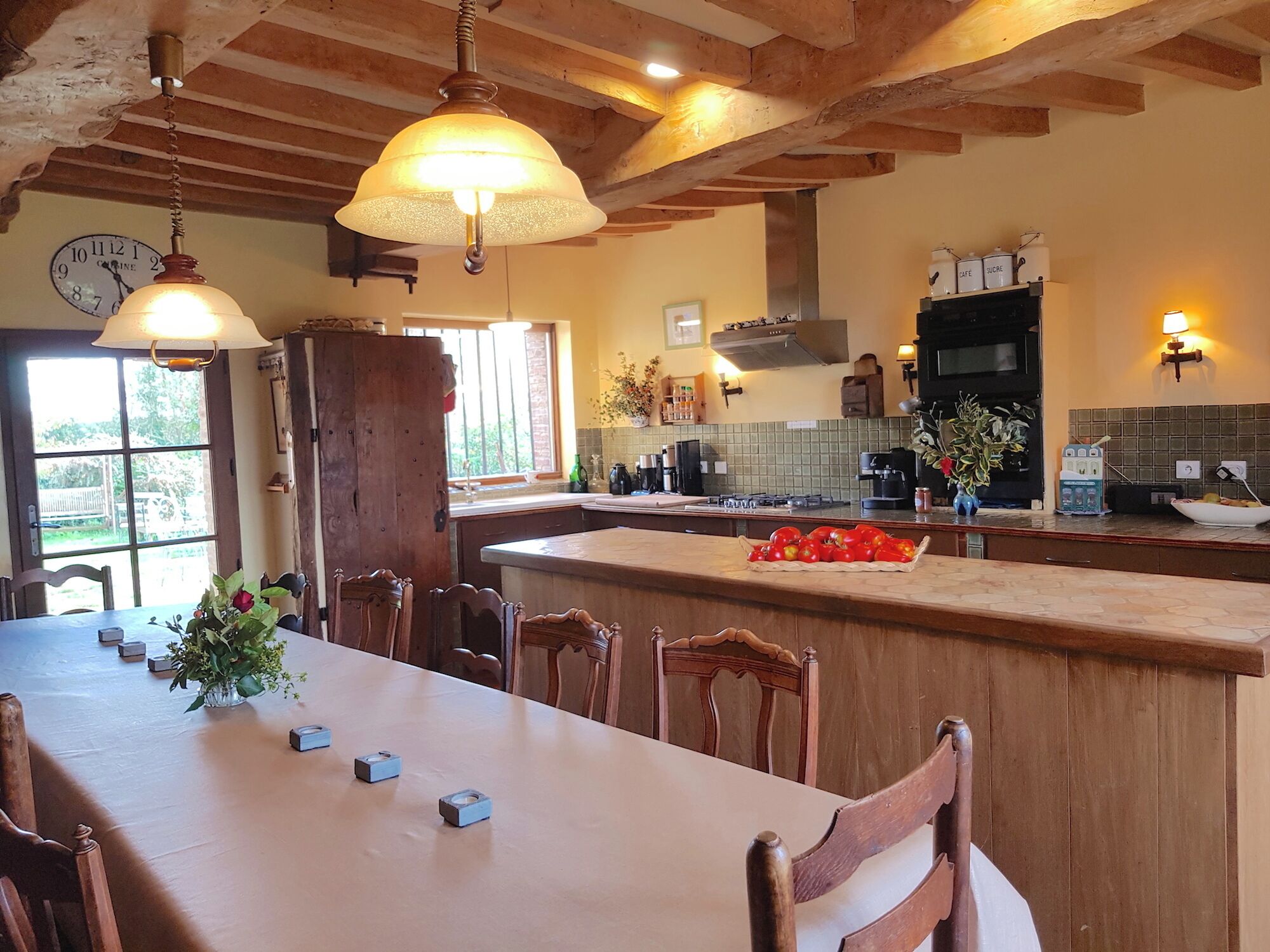 Une cuisine dotée d’un îlot central, de chaises en bois, d’une table à manger et de luminaires suspendus.
