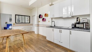 A modern kitchen with white cabinets, a wooden dining table, and a black microwave. - Modern Flat - 2ch/6p - Bastille (Paris)