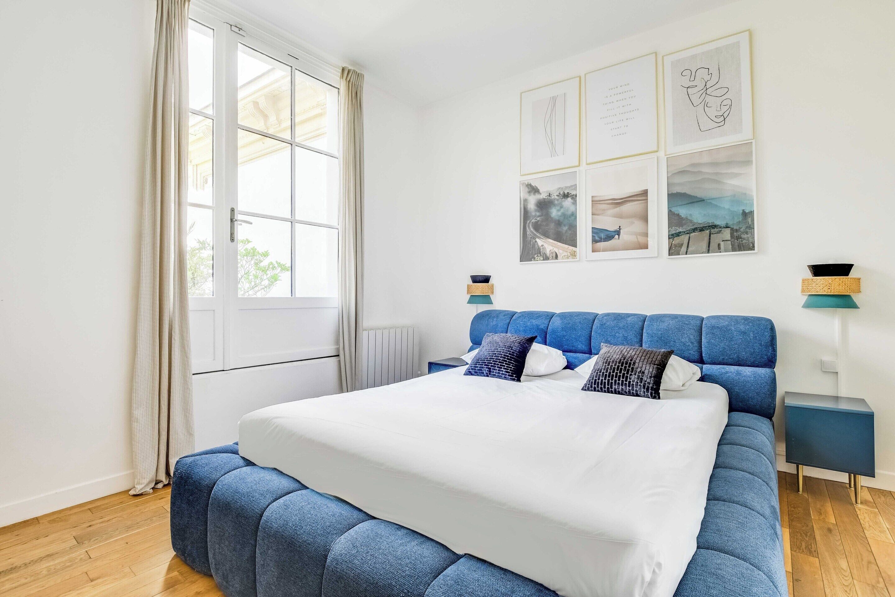 Une chambre avec un grand lit, une fenêtre avec des rideaux, une table de chevet et des œuvres d’art murales.