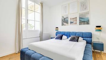 Une chambre avec un grand lit, une fenêtre avec des rideaux, une table de chevet et des œuvres d’art murales.