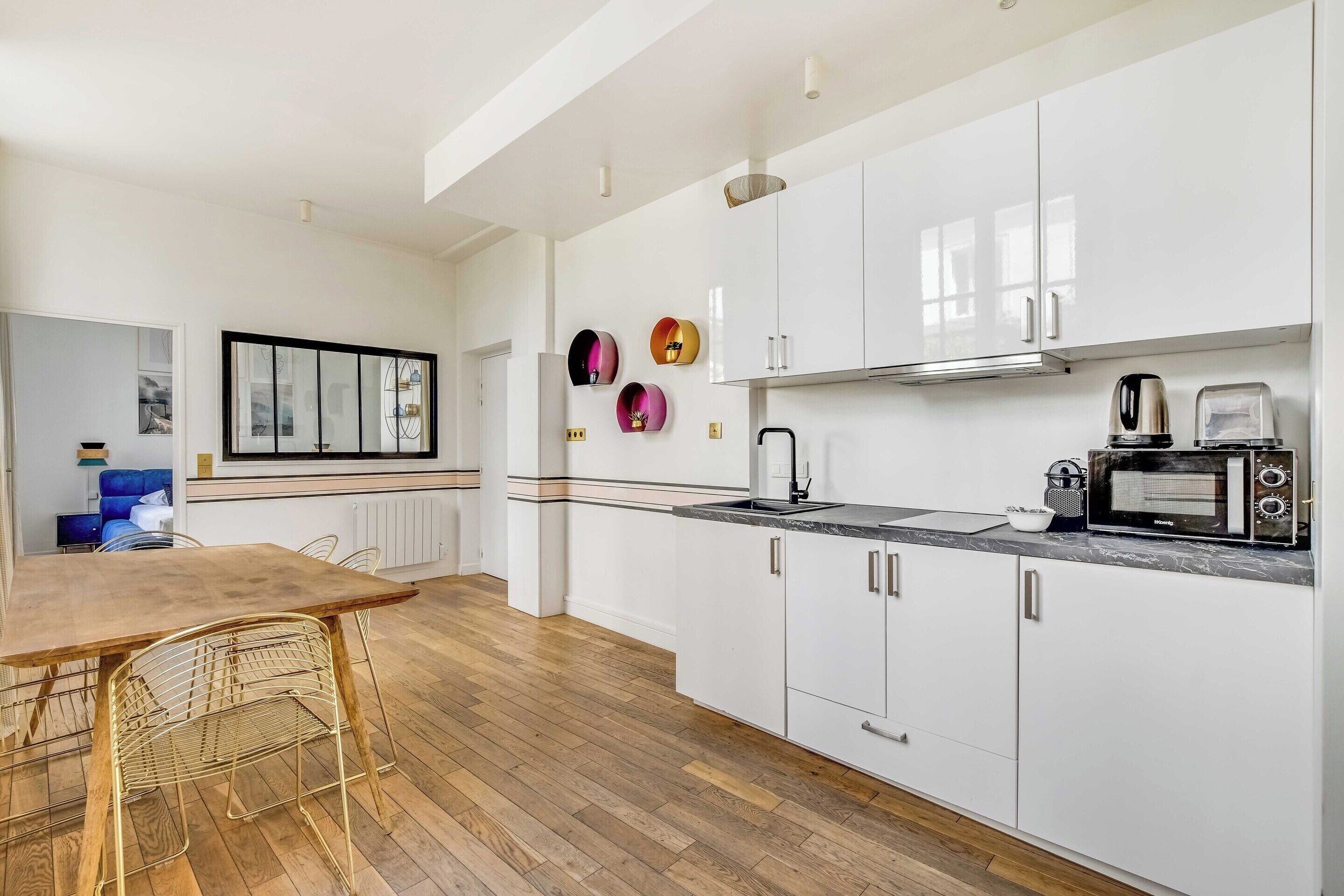 Une cuisine moderne avec des meubles blancs, une table à manger en bois et un micro-ondes noir.