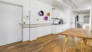 A modern kitchen with white cabinets, a wooden dining table, and a built-in oven. - Modern Flat - 2ch/6p - Bastille (Paris)