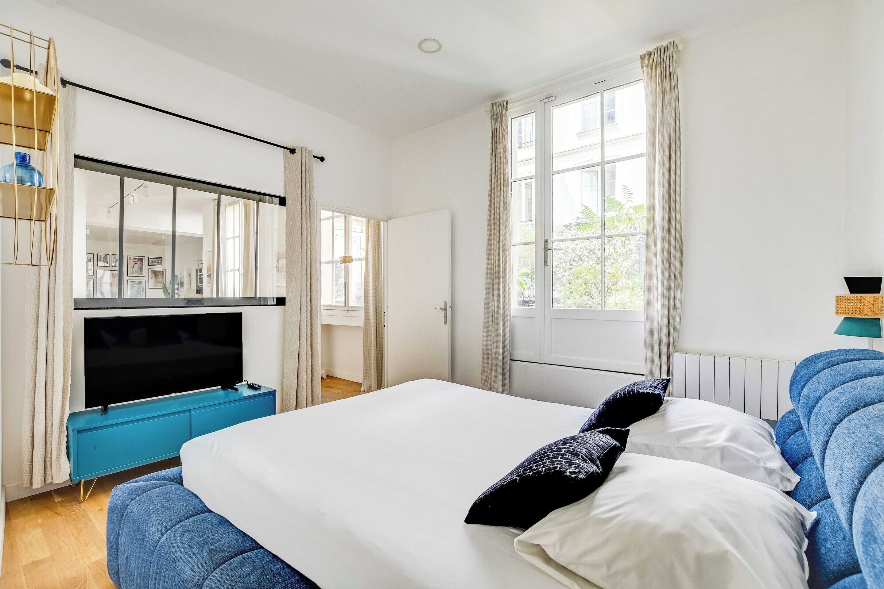 A bedroom with a bed, a TV, and a window with curtains.