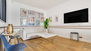 A modern living room with a white sofa, a coffee table, a TV mounted on the wall, and a series of framed pictures. - Modern Flat - 2ch/6p - Bastille (Paris)